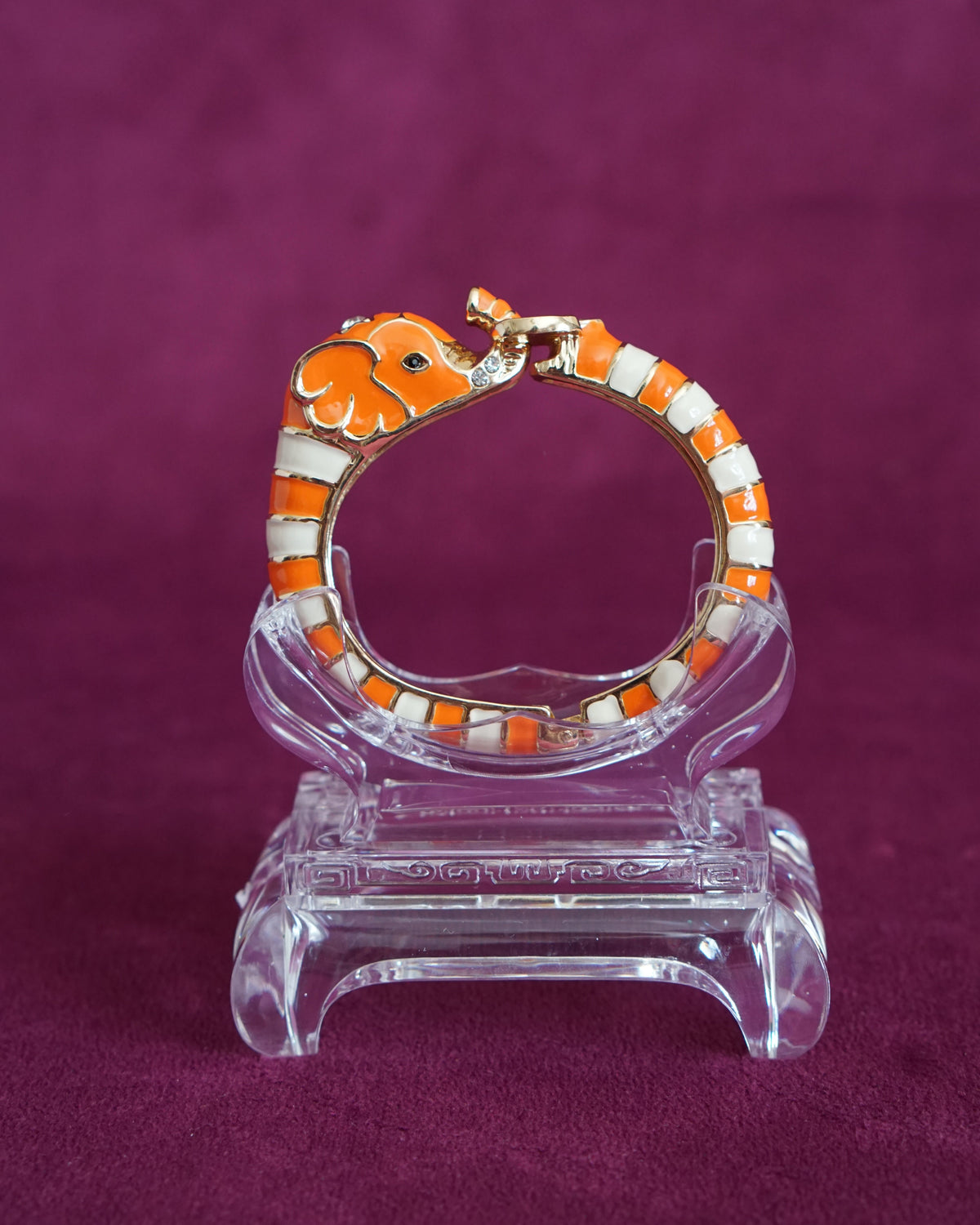 Hinged orange and cream enamel bangle shaped like an elephant curling around the wrist