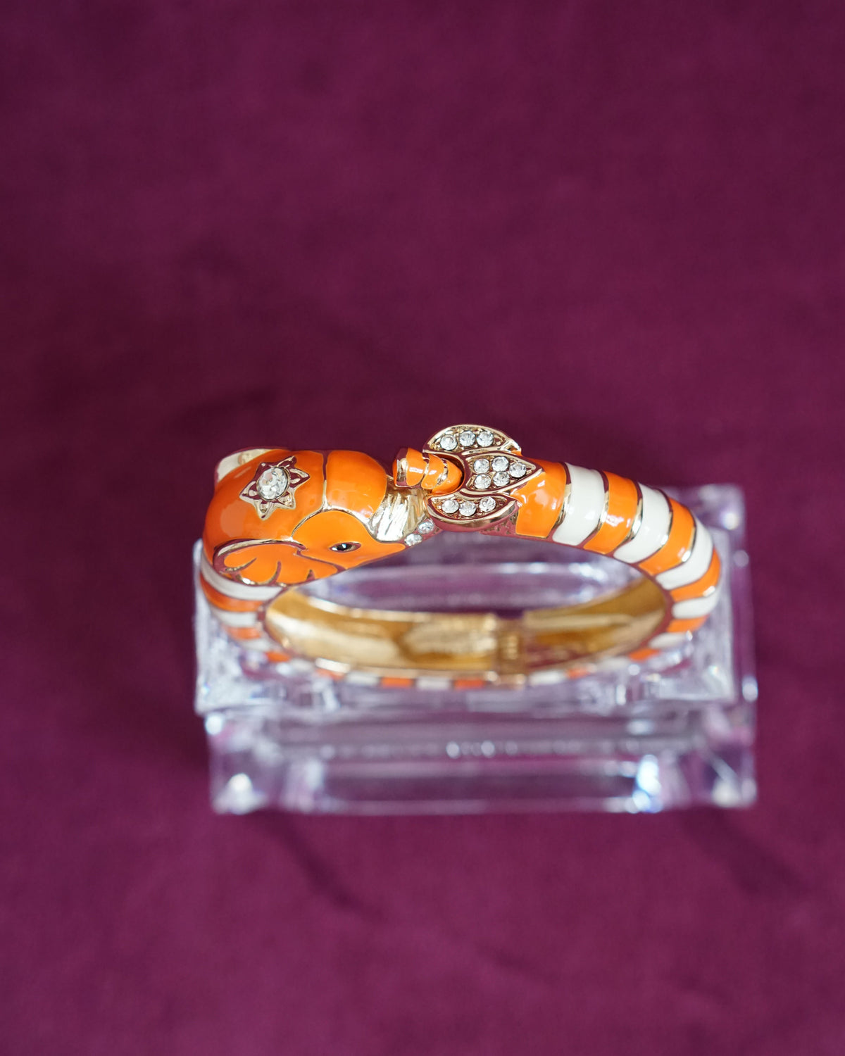 Hinged orange and cream enamel bangle shaped like an elephant curling around the wrist