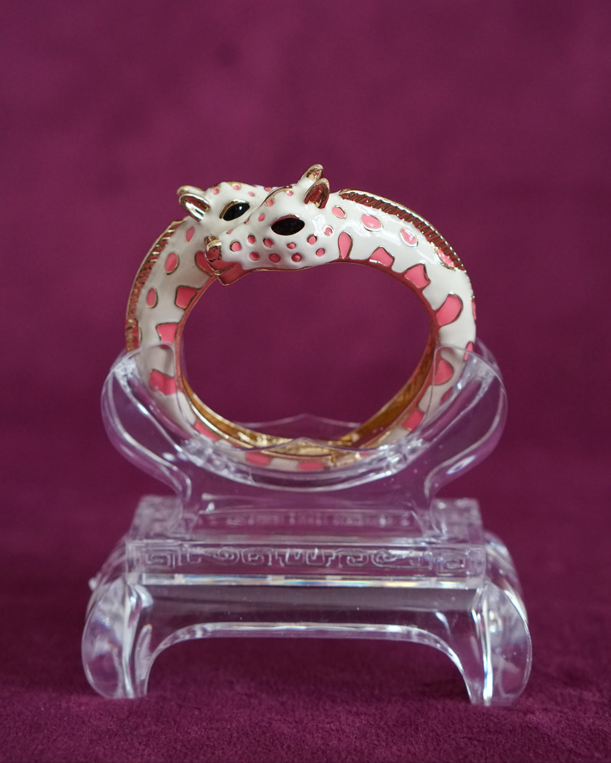 Hinged cream enamel bangle with two giraffes nuzzling at the front of the wrist, soft pink accents