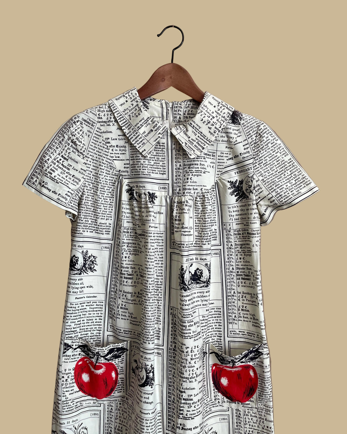 A vintage handmade shift dress with an apple and farmer's-almanac newspaper print, shown against a kraft background