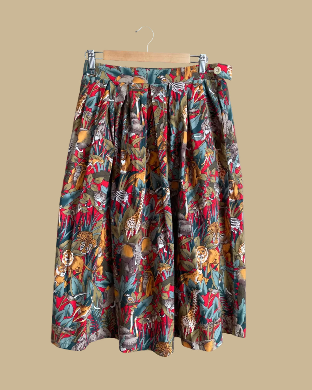 A vintage handmade pleated midi skirt with a jungle safari animal print featuring elephants, giraffes, zebras, and tigers in red, olive, and teal, shown against a kraft background