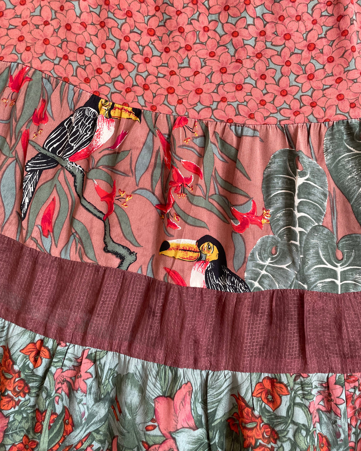 A vintage Carole Little tiered silk skirt with a tropical toucan and floral print in brown, teal, and orange tones, shown against a kraft background