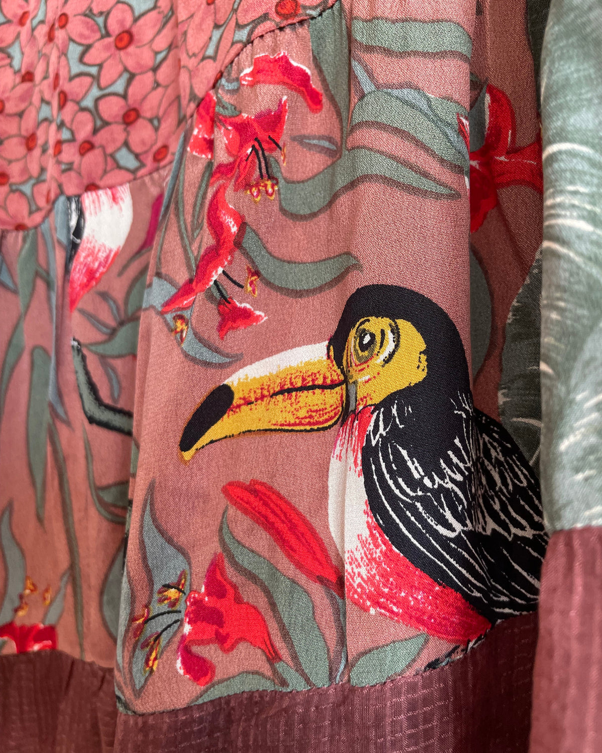 A vintage Carole Little tiered silk skirt with a tropical toucan and floral print in brown, teal, and orange tones, shown against a kraft background