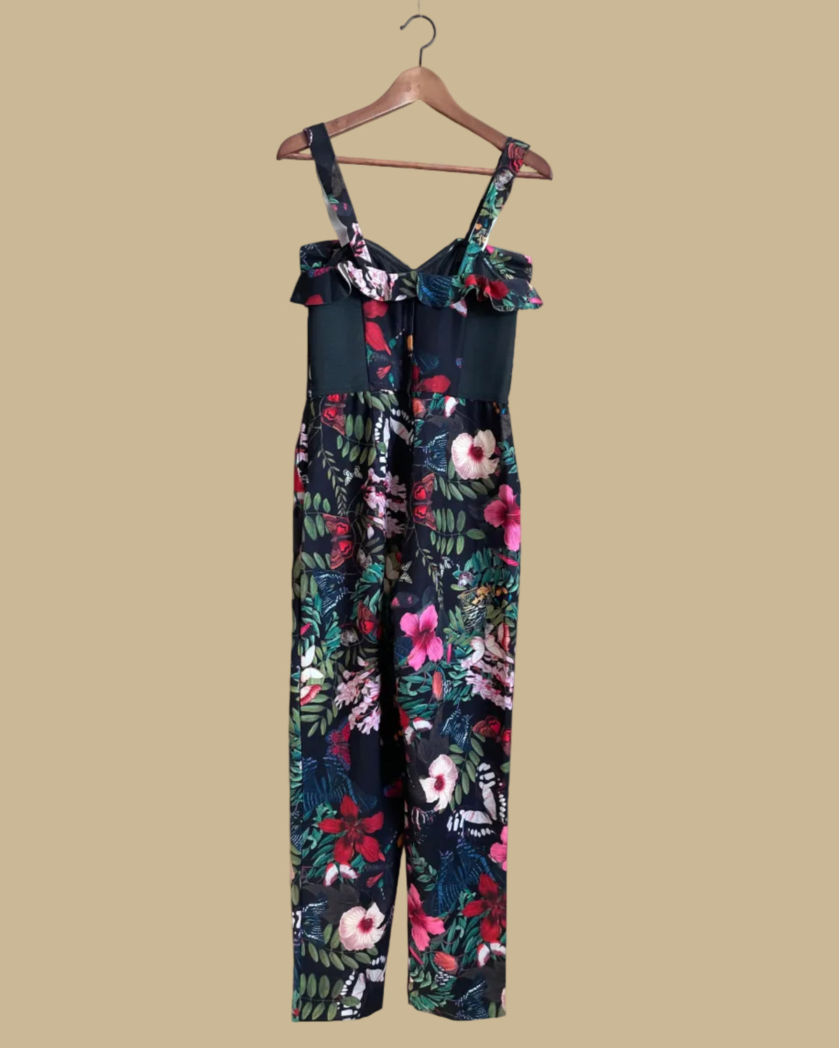 An H&M botanical and butterfly print jumpsuit with ruffle-trimmed straps on a black ground, shown against a kraft background