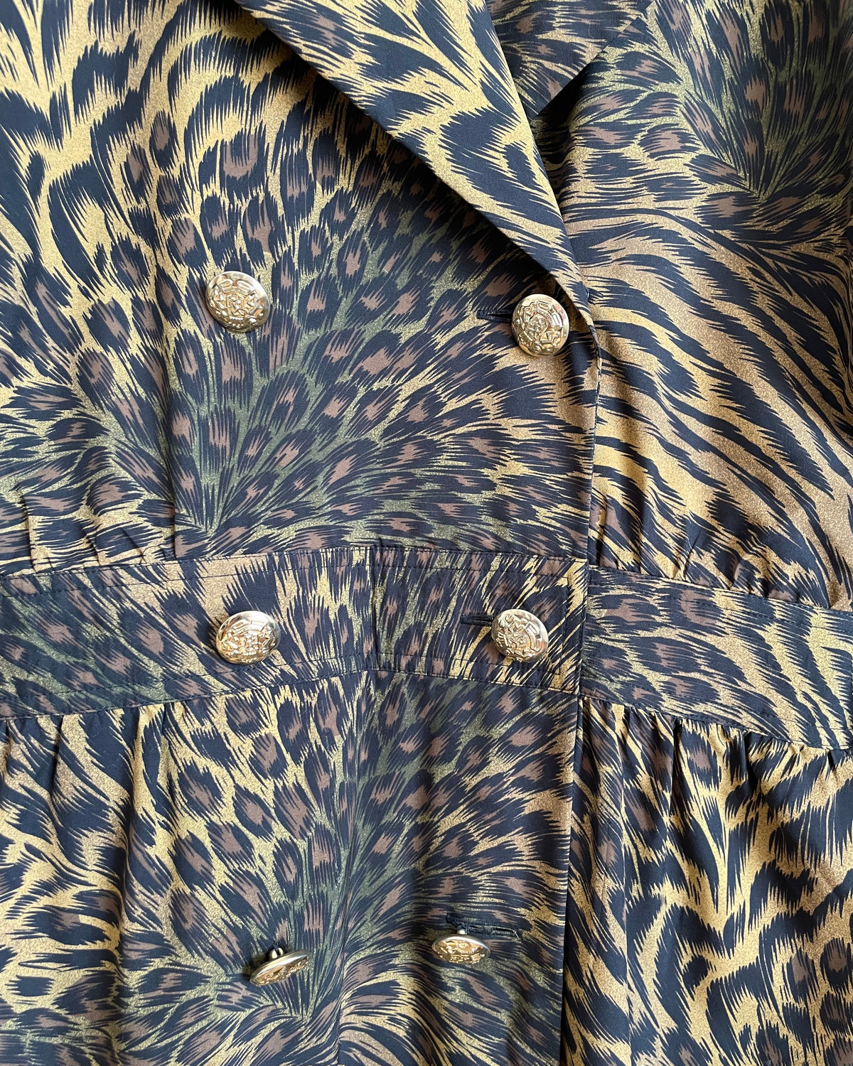 A vintage Leslie Fay double-breasted animal print dress with gold lion-head buttons and epaulette detail, shown against a kraft background