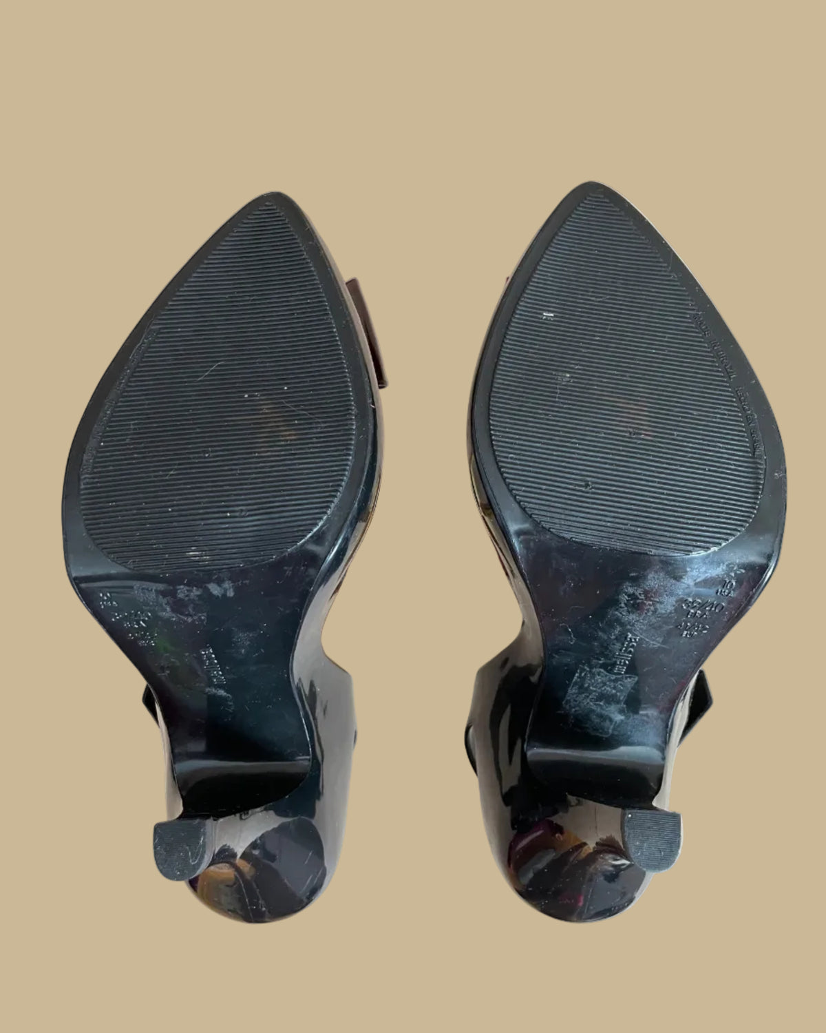 A pair of black jelly slingback heels from the Vivienne Westwood Anglomania x Melissa collaboration with a tortoiseshell bow, displayed on gold stands against a kraft background