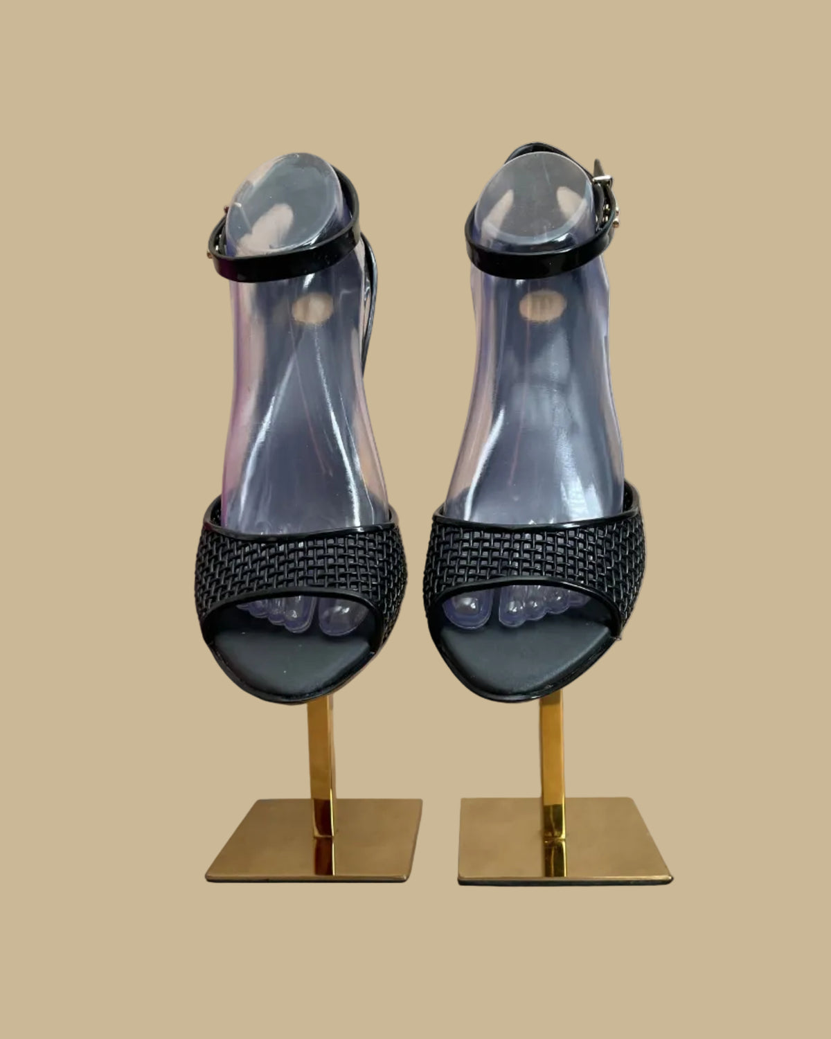 A pair of black Melissa jelly wedge sandals with a woven-texture toe strap and ankle buckle, displayed on gold stands against a kraft background