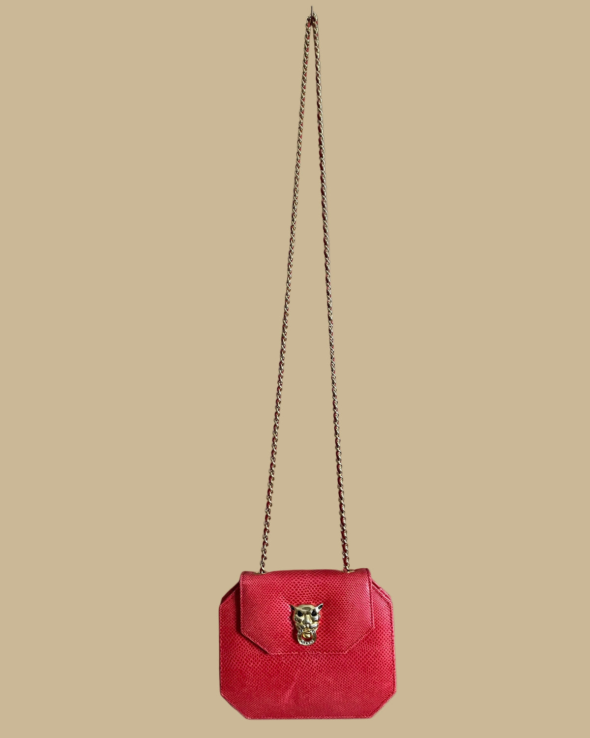 A small red textured snakeskin handbag with a gold-tone panther head clasp, shown on a neutral beige background with its matching chain strap