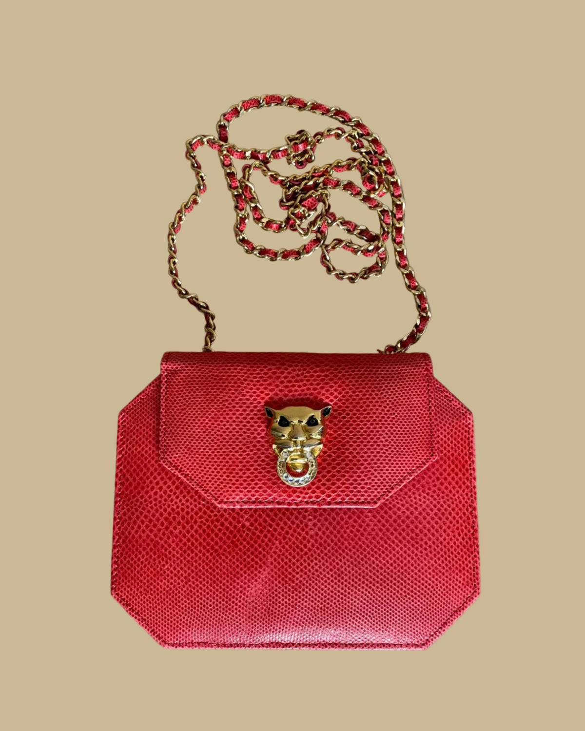 A small red textured snakeskin handbag with a gold-tone panther head clasp, shown on a neutral beige background with its matching chain strap