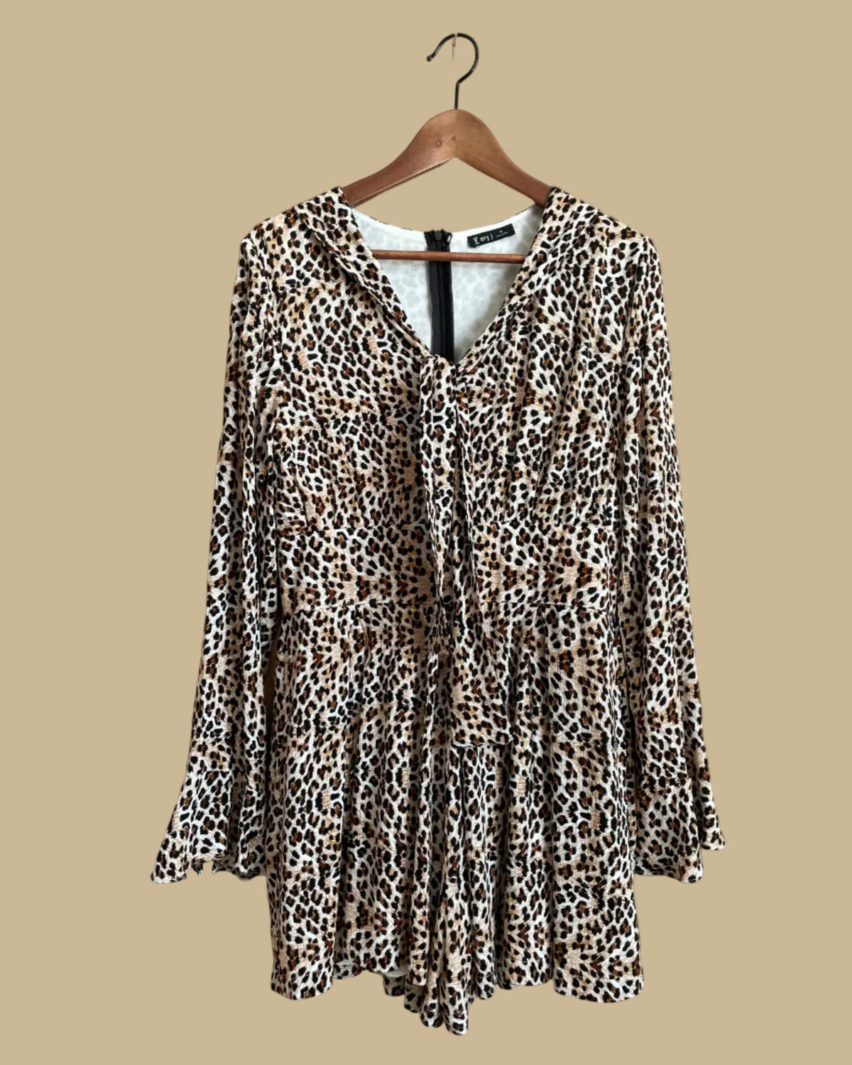 A Very J leopard print romper with a tie-neck V and bell sleeves, shown against a kraft background