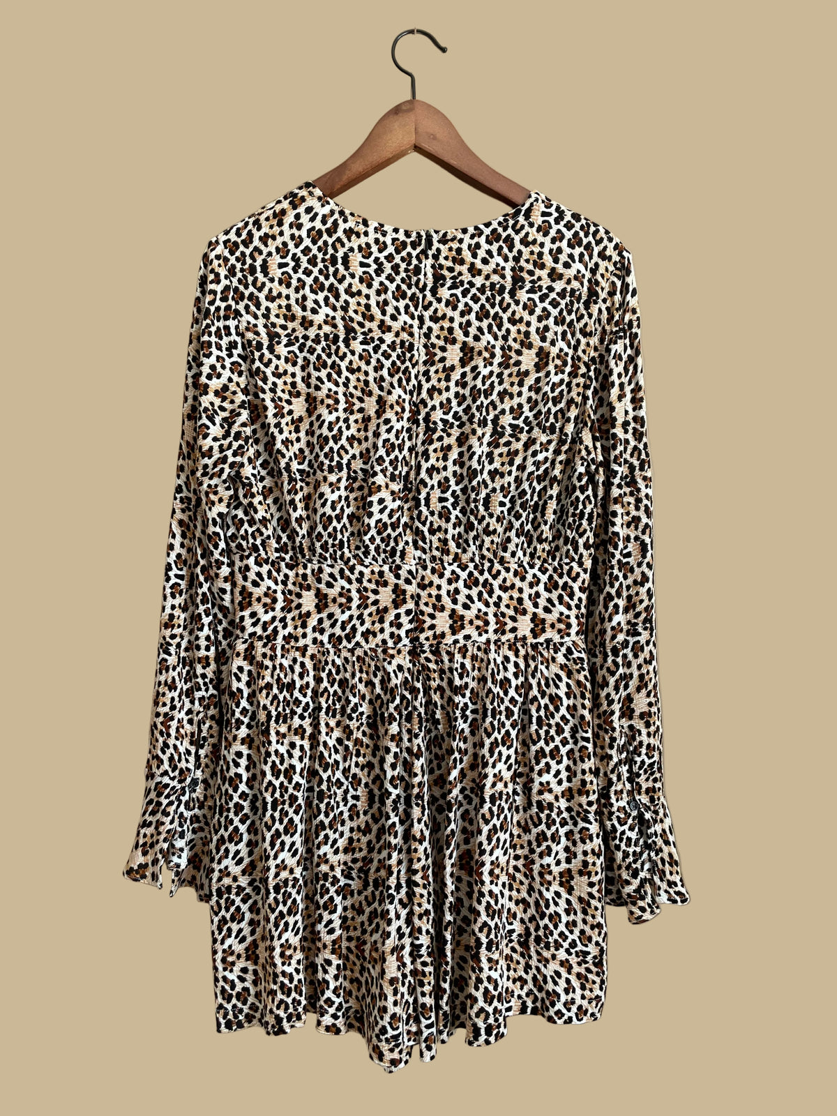 A Very J leopard print romper with a tie-neck V and bell sleeves, shown against a kraft background