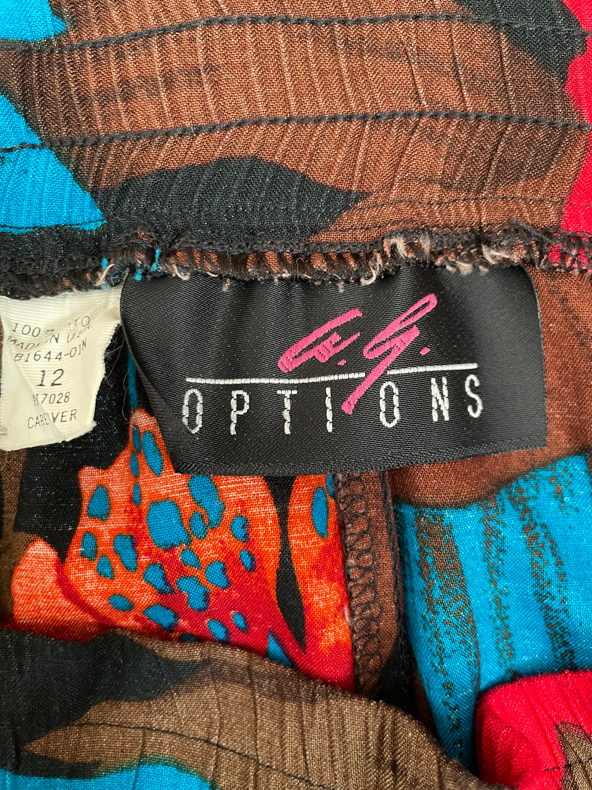 A vintage tropical bird-of-paradise print pleated skirt in brown, black, teal, and orange tones, shown against a kraft background
