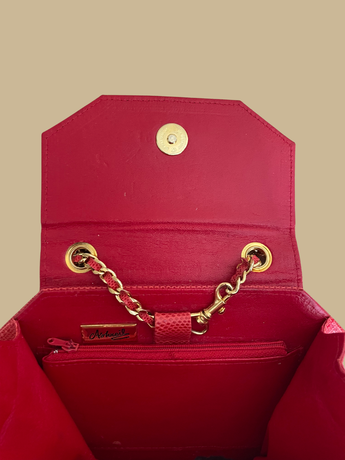 A small red textured snakeskin handbag with a gold-tone panther head clasp, shown on a neutral beige background with its matching chain strap