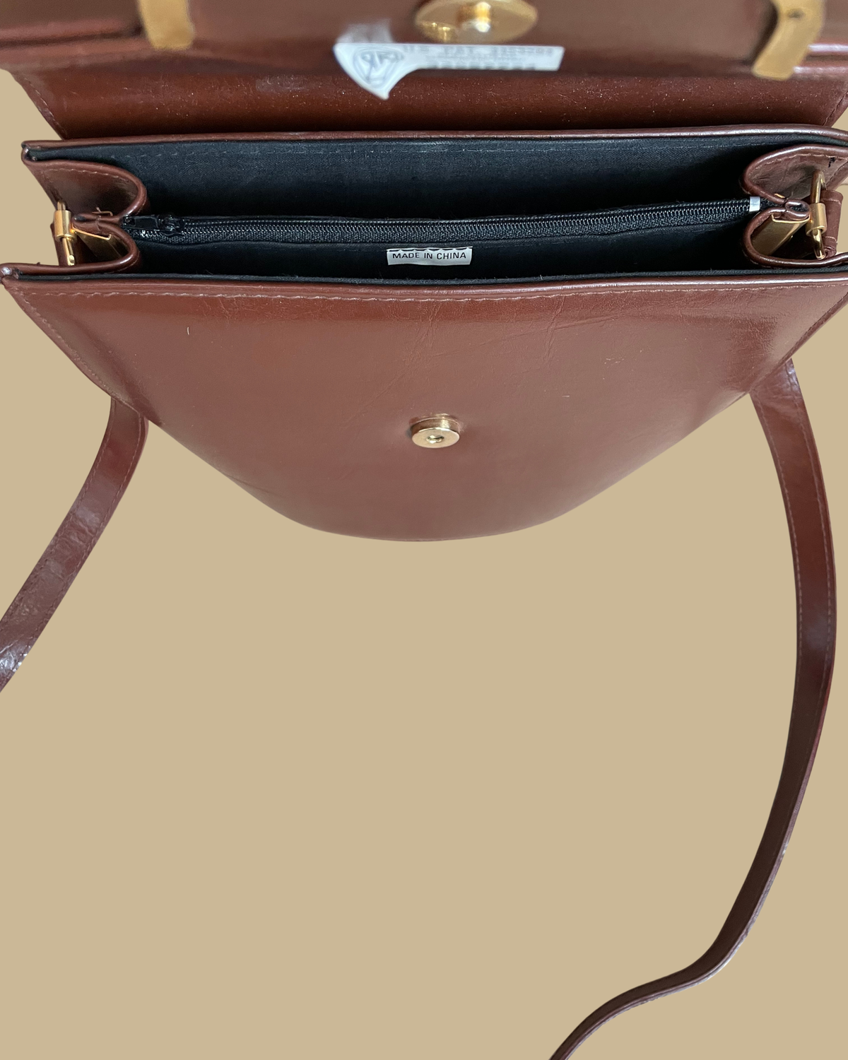 A vintage brown crossbody bag with a sculptural gold-tone and black enamel zebra clasp on the flap closure, shown against a kraft background