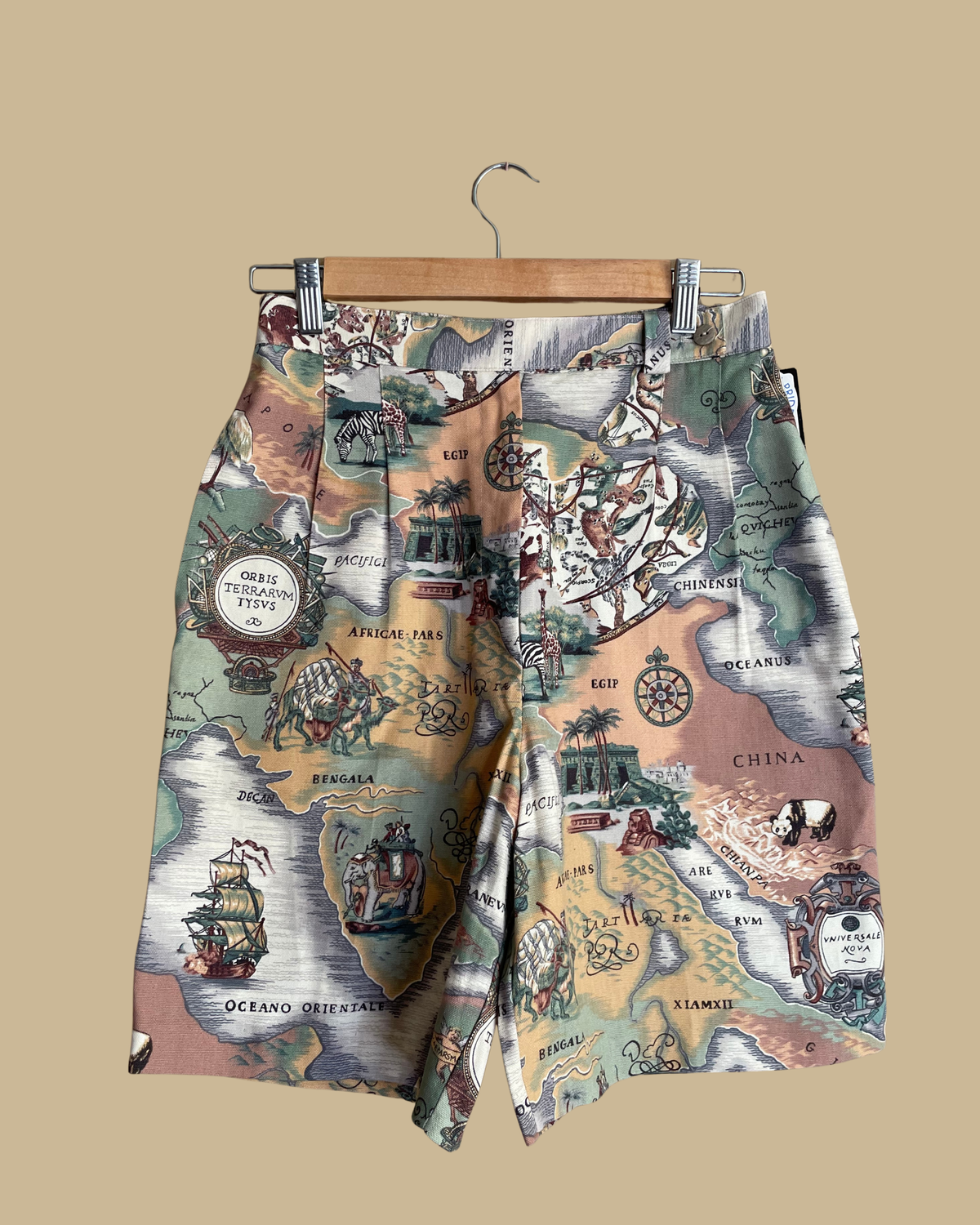Vintage map cartography print high-waisted shorts on a hanger, featuring zebras, giraffes, elephants, and ships against a beige background