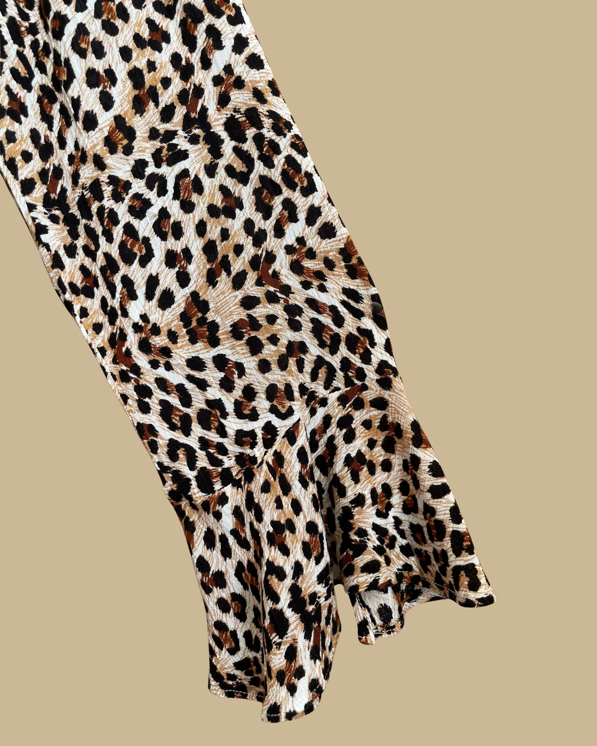 A Very J leopard print romper with a tie-neck V and bell sleeves, shown against a kraft background