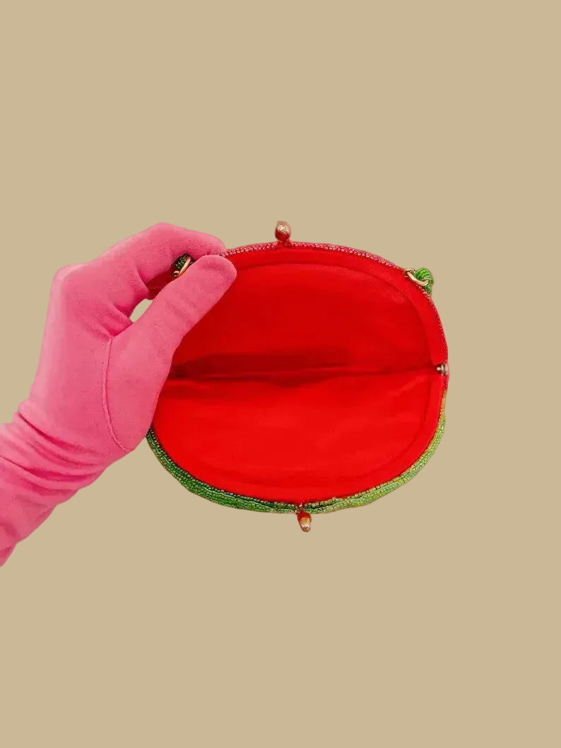 Red round pouch with green trim held open by a pink gloved hand on a white background