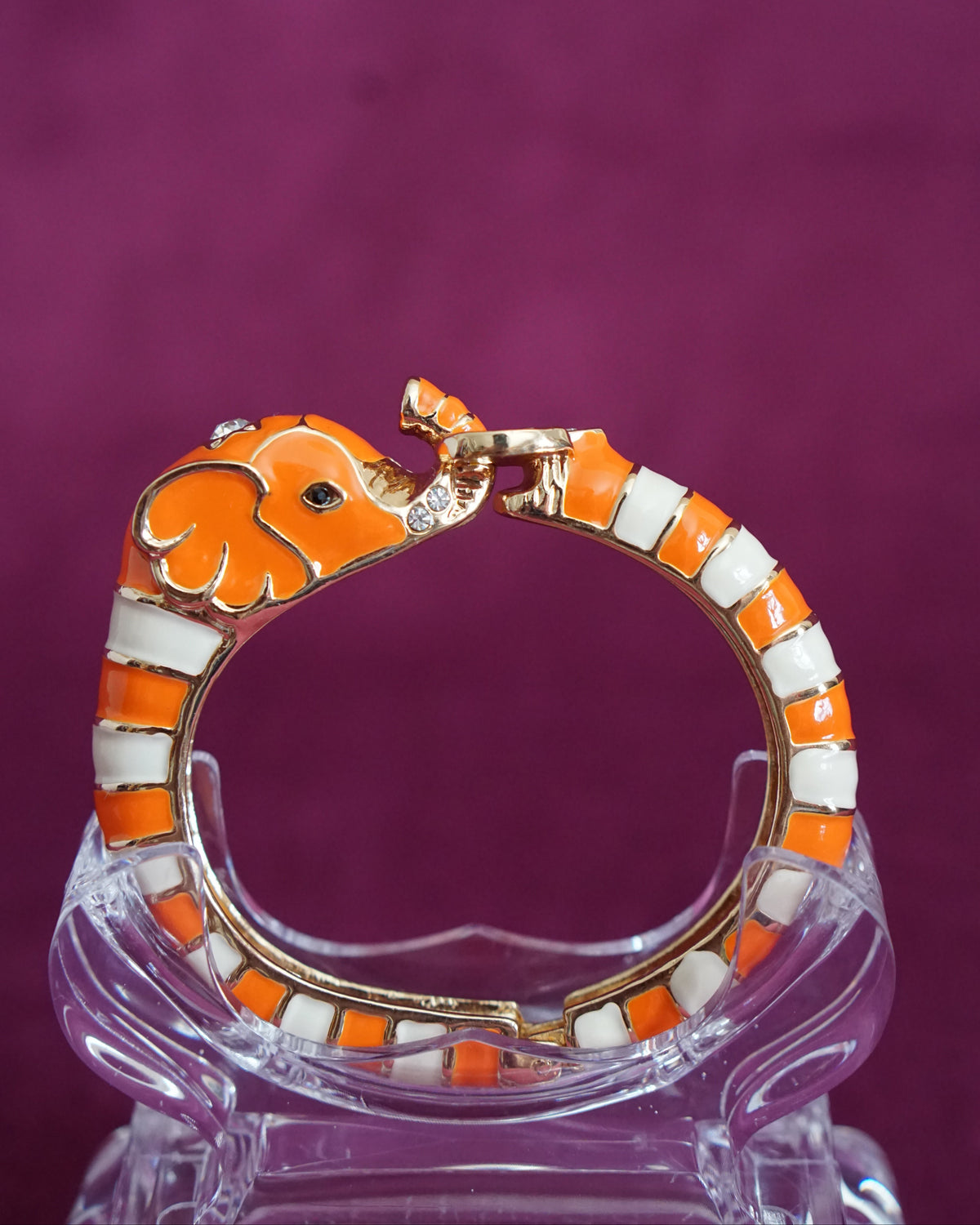 Hinged orange and cream enamel bangle shaped like an elephant curling around the wrist