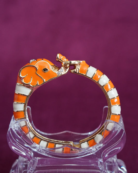 Hinged orange and cream enamel bangle shaped like an elephant curling around the wrist