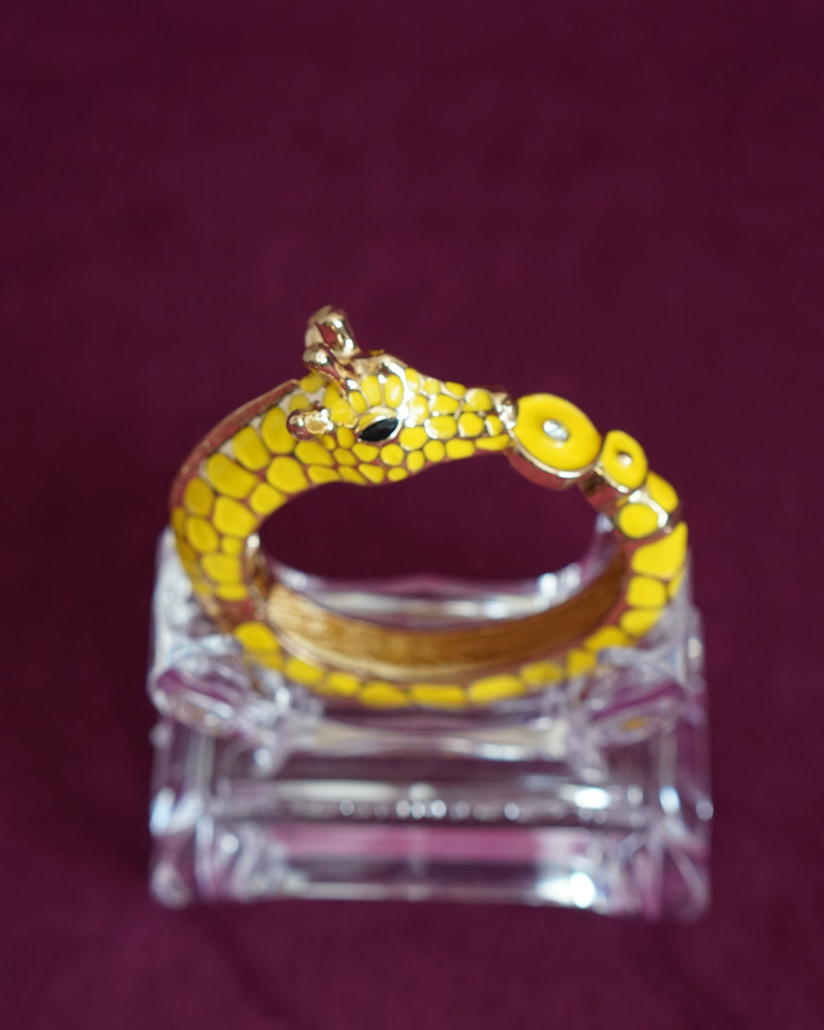 Sculptural hinged bangle shaped like a giraffe wrapping around the wrist, in sunny yellow enamel