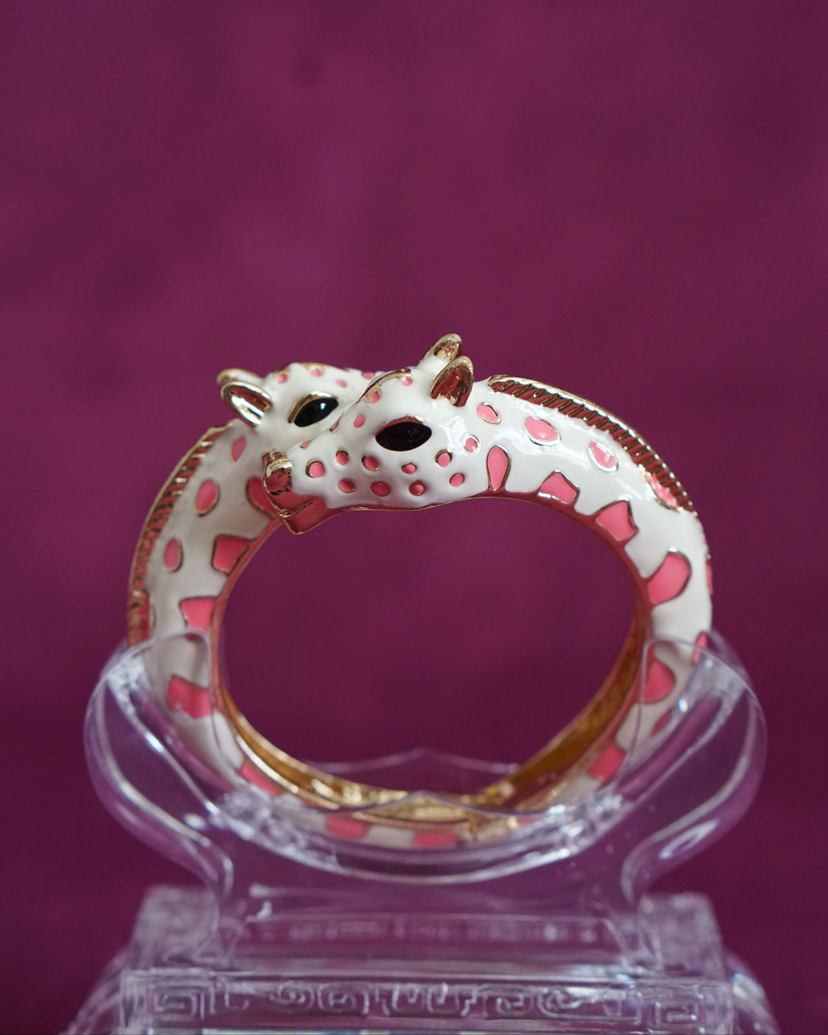 Hinged cream enamel bangle with two giraffes nuzzling at the front of the wrist, soft pink accents
