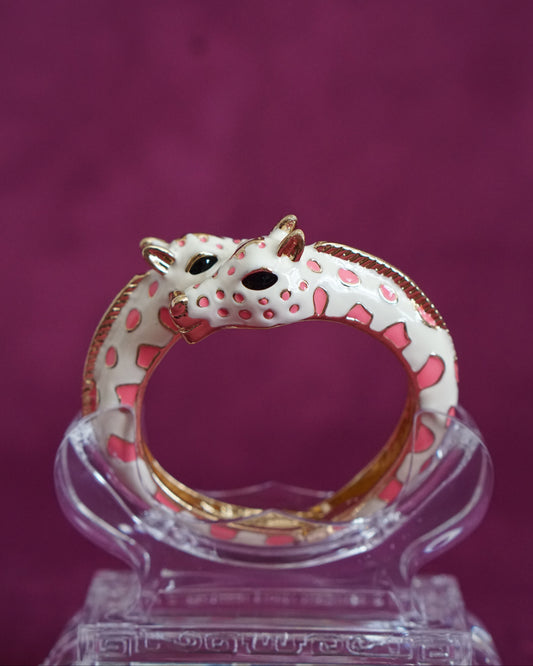 Hinged cream enamel bangle with two giraffes nuzzling at the front of the wrist, soft pink accents