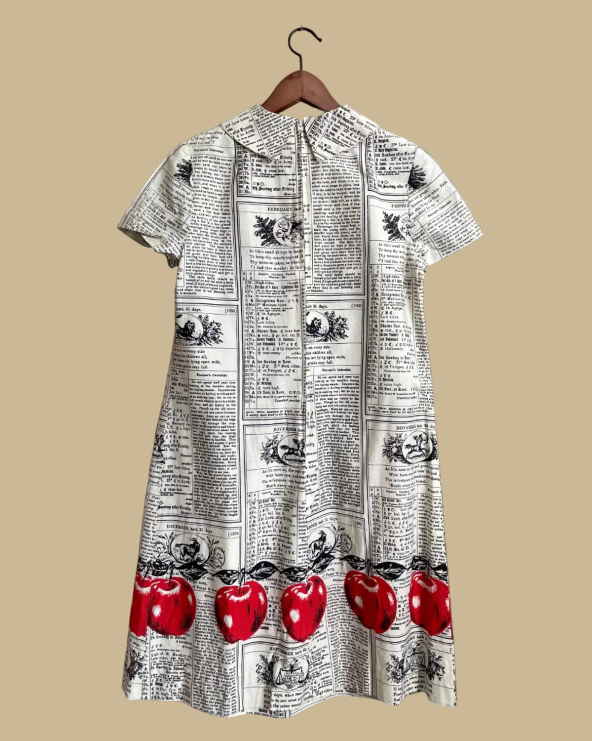 A vintage handmade shift dress with an apple and farmer's-almanac newspaper print, shown against a kraft background