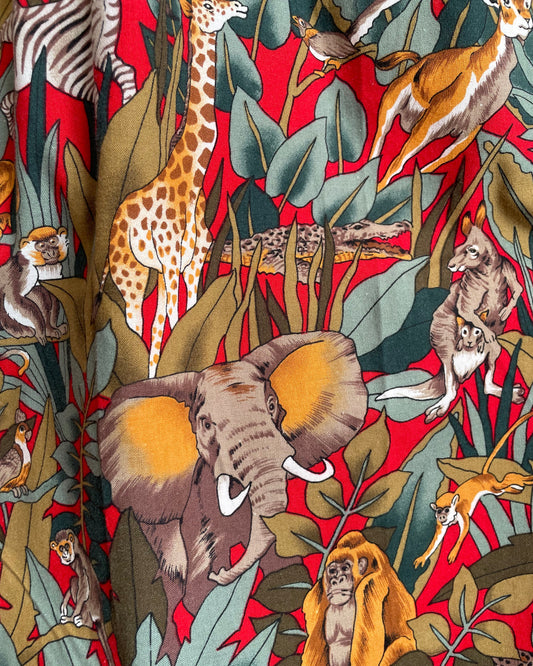 A vintage handmade pleated midi skirt with a jungle safari animal print featuring elephants, giraffes, zebras, and tigers in red, olive, and teal, shown against a kraft background