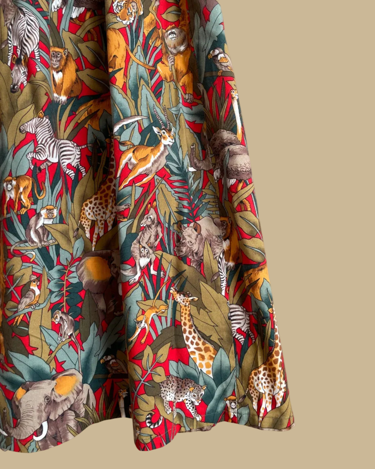 A vintage handmade pleated midi skirt with a jungle safari animal print featuring elephants, giraffes, zebras, and tigers in red, olive, and teal, shown against a kraft background
