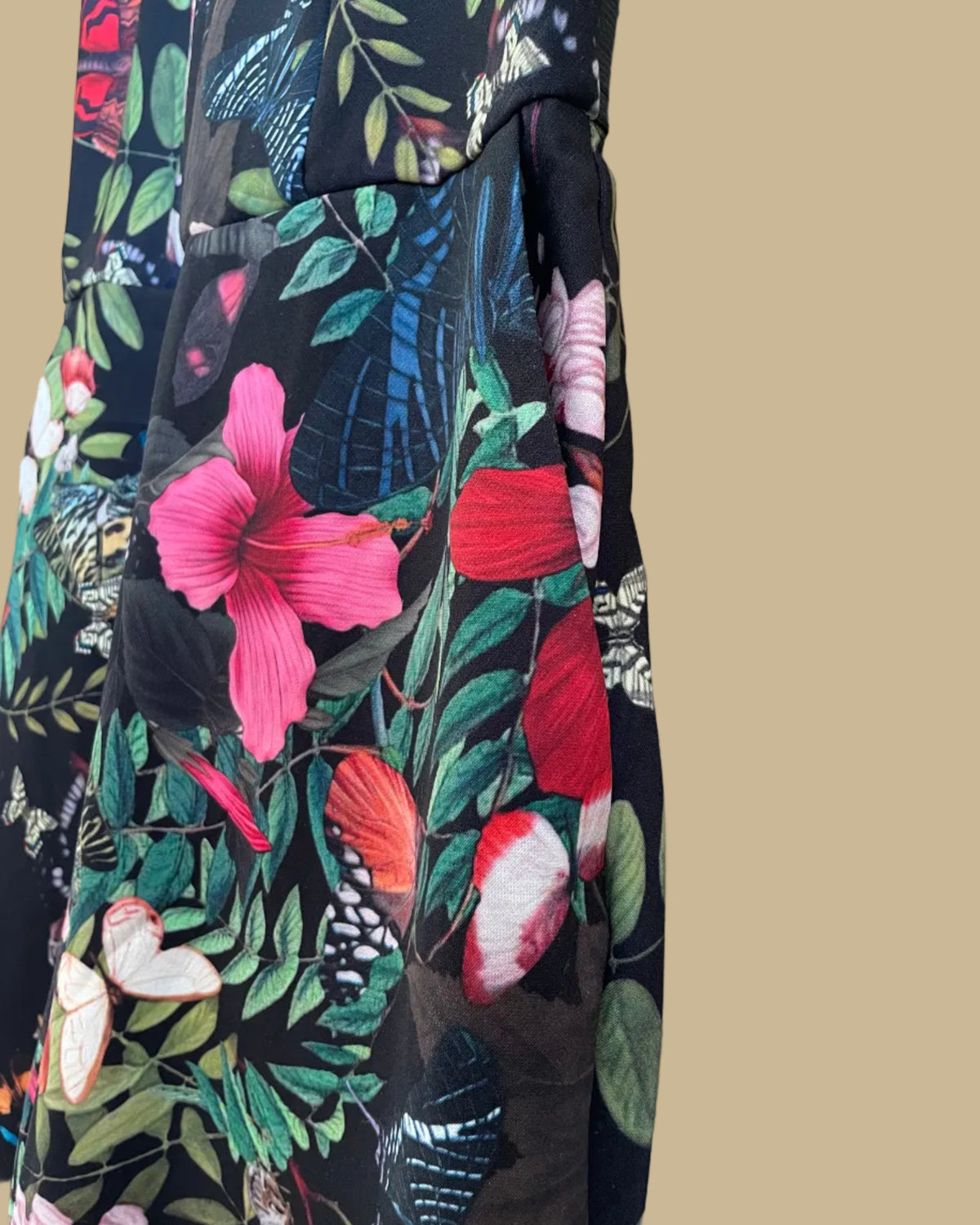 An H&M botanical and butterfly print jumpsuit with ruffle-trimmed straps on a black ground, shown against a kraft background