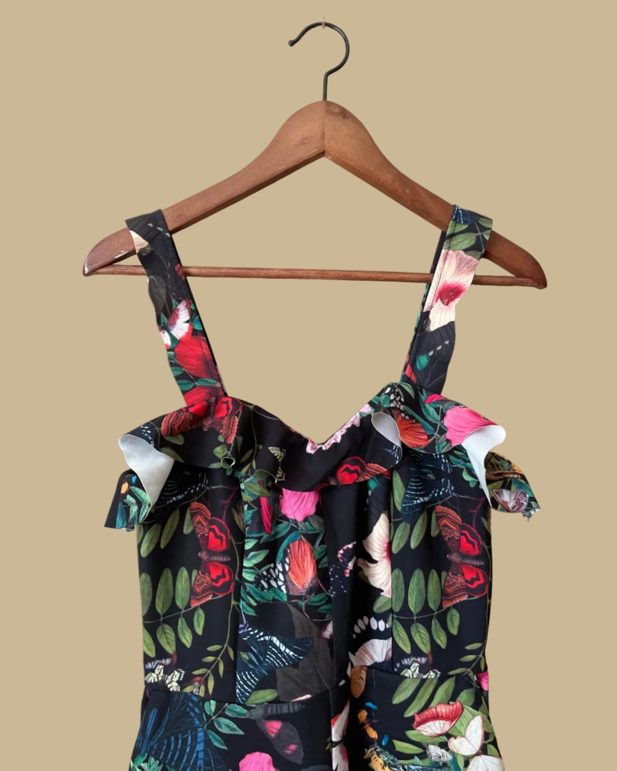 An H&M botanical and butterfly print jumpsuit with ruffle-trimmed straps on a black ground, shown against a kraft background