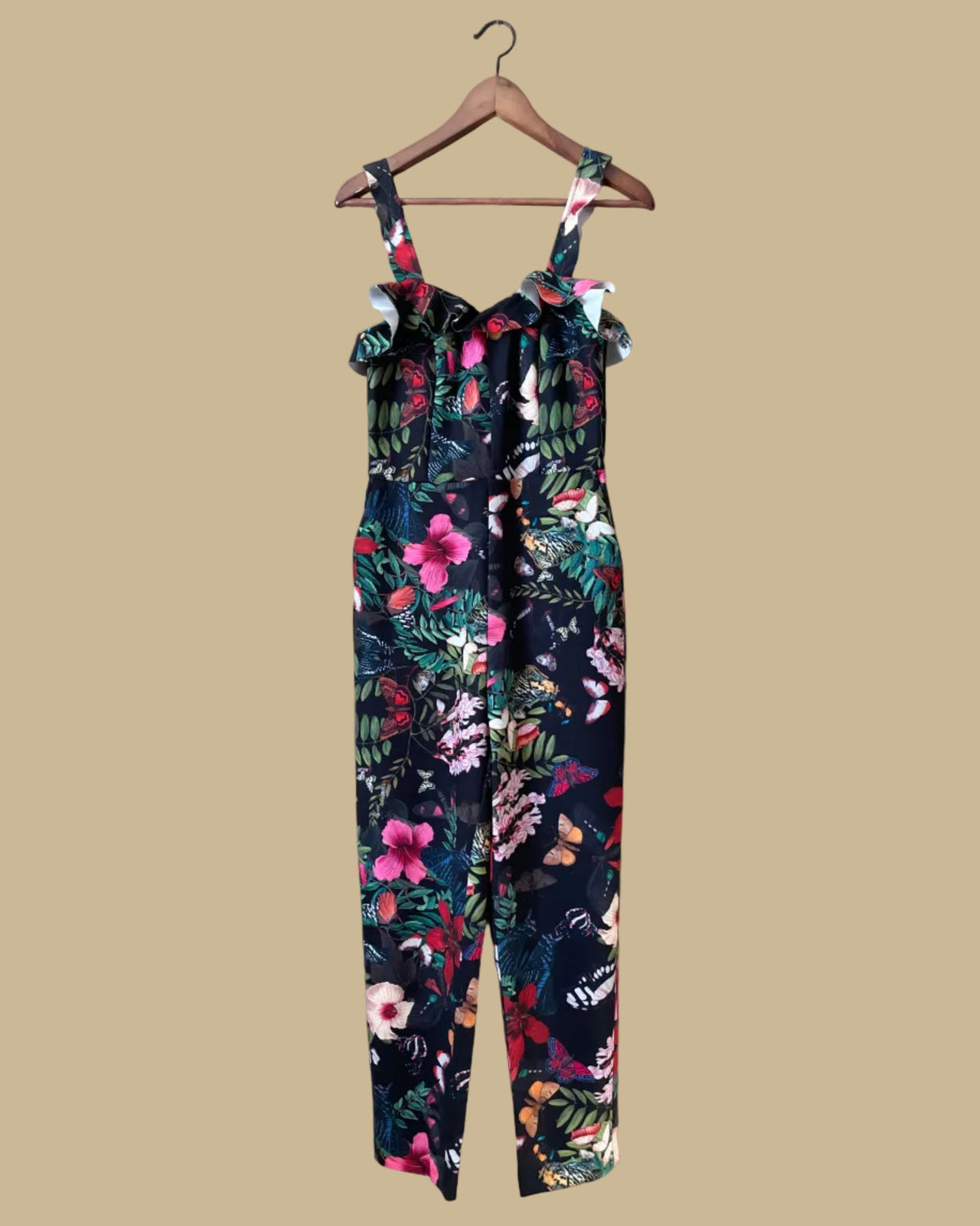 An H&M botanical and butterfly print jumpsuit with ruffle-trimmed straps on a black ground, shown against a kraft background