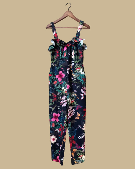 An H&M botanical and butterfly print jumpsuit with ruffle-trimmed straps on a black ground, shown against a kraft background
