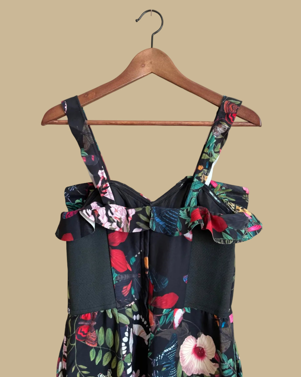 An H&M botanical and butterfly print jumpsuit with ruffle-trimmed straps on a black ground, shown against a kraft background