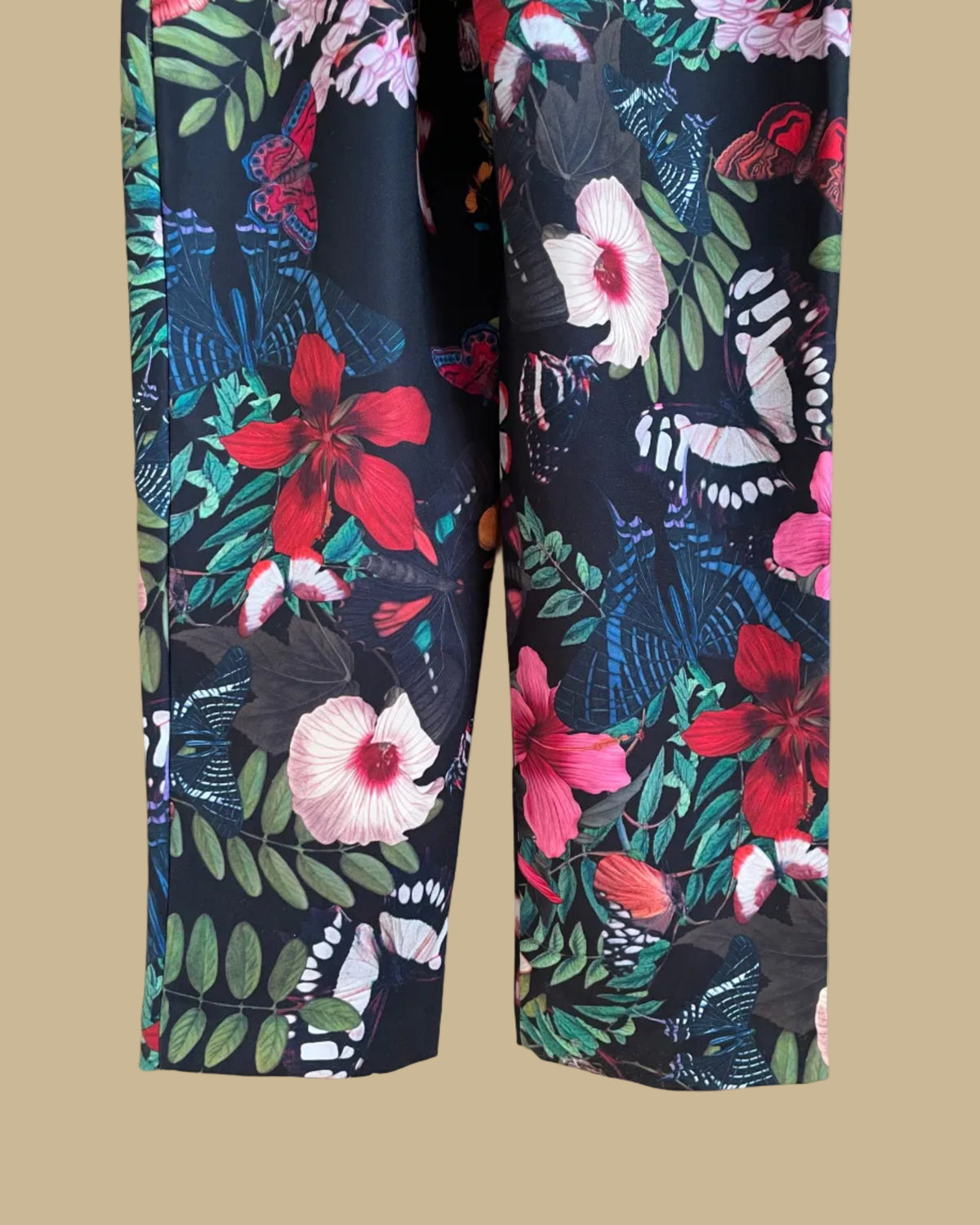 An H&M botanical and butterfly print jumpsuit with ruffle-trimmed straps on a black ground, shown against a kraft background