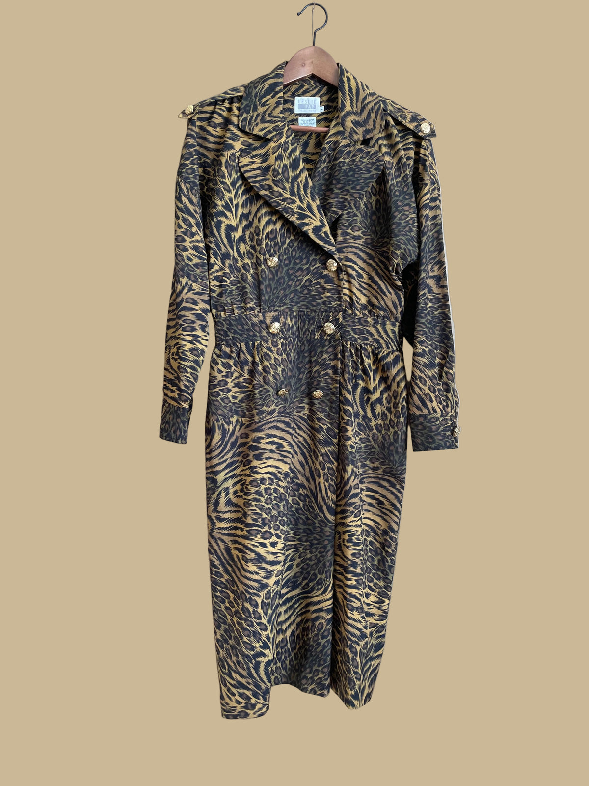 A vintage Leslie Fay double-breasted animal print dress with gold lion-head buttons and epaulette detail, shown against a kraft background