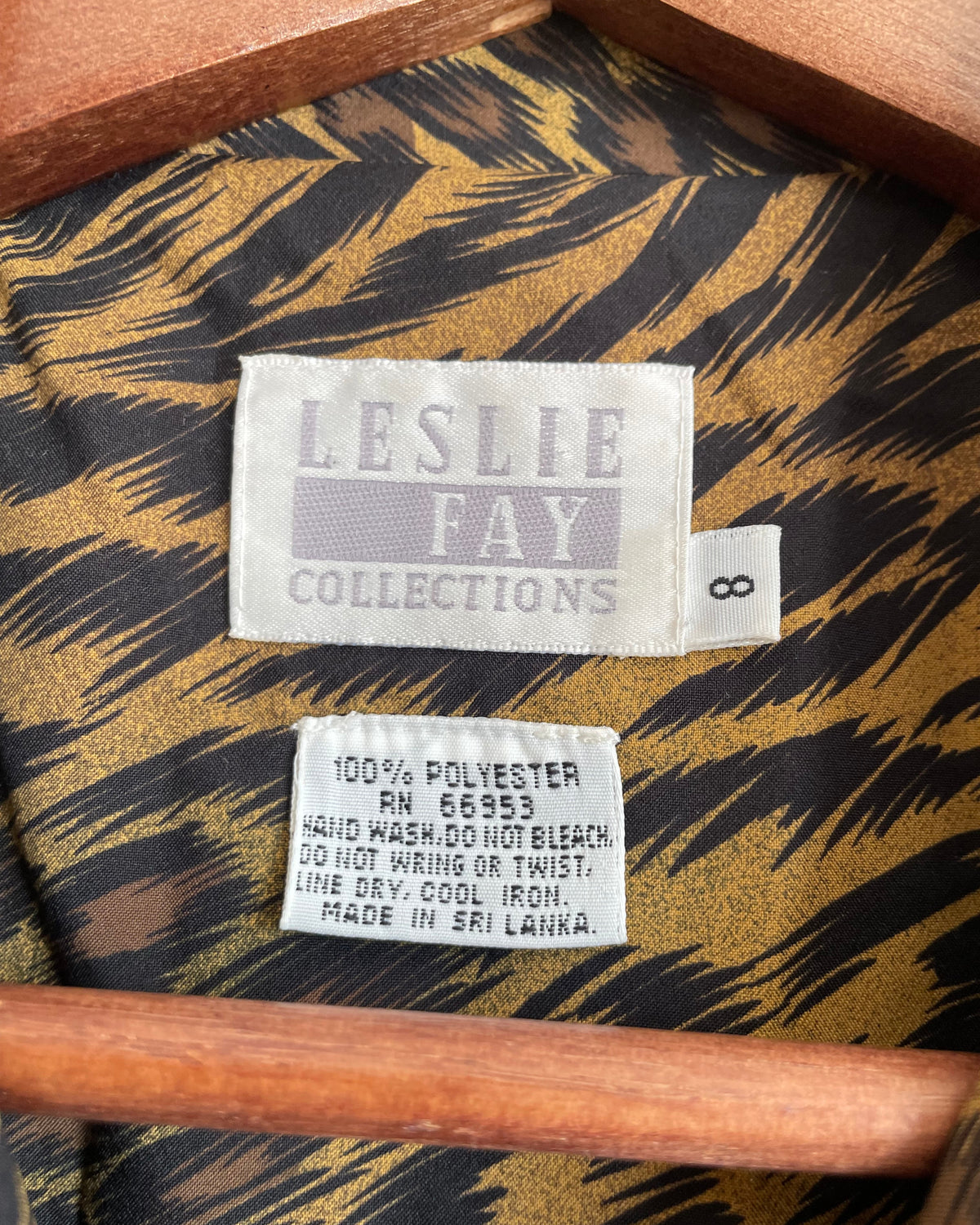 A vintage Leslie Fay double-breasted animal print dress with gold lion-head buttons and epaulette detail, shown against a kraft background