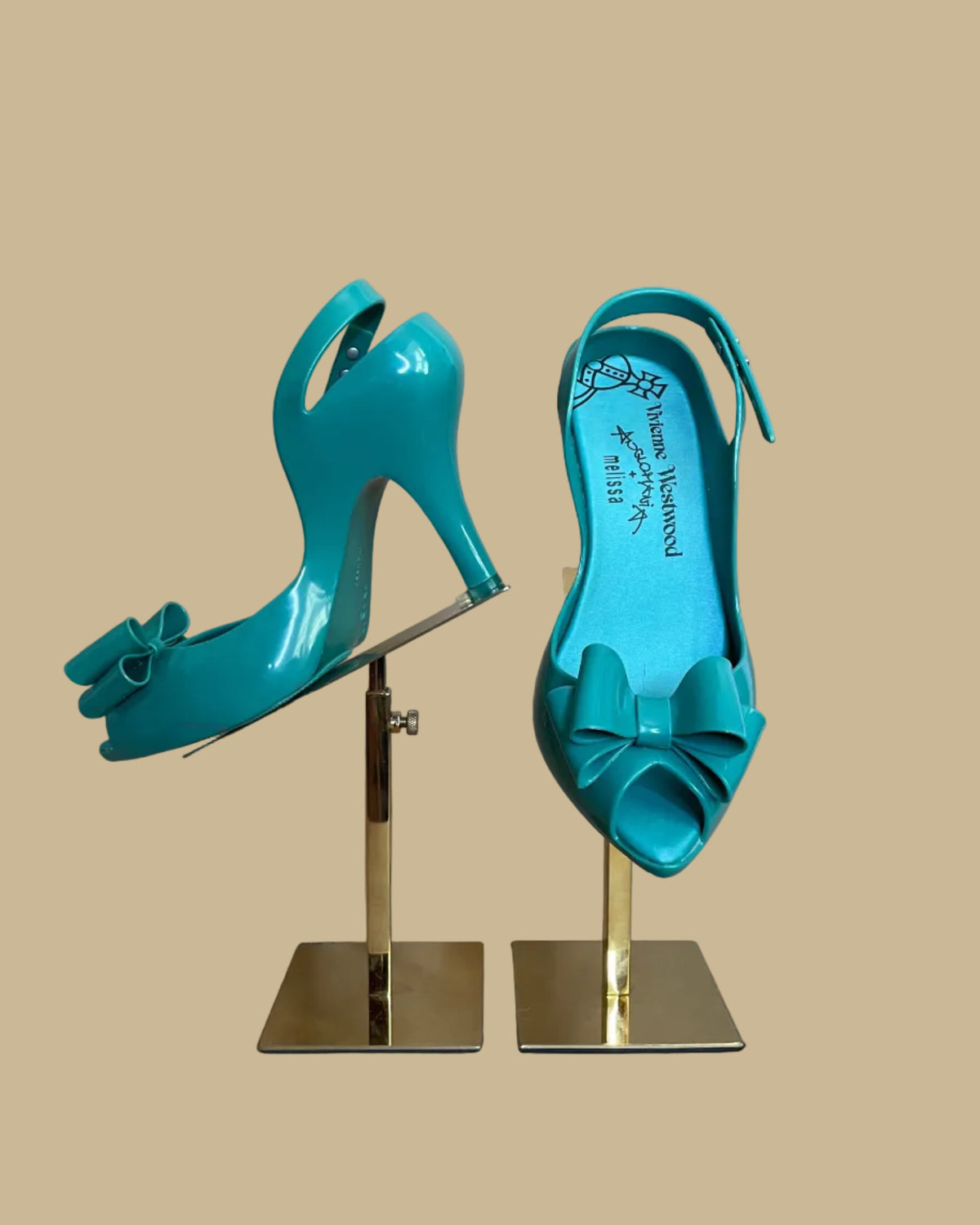 Vivienne Westwood Anglomania and Melissa teal jelly bow heels displayed on gold stands against a beige background