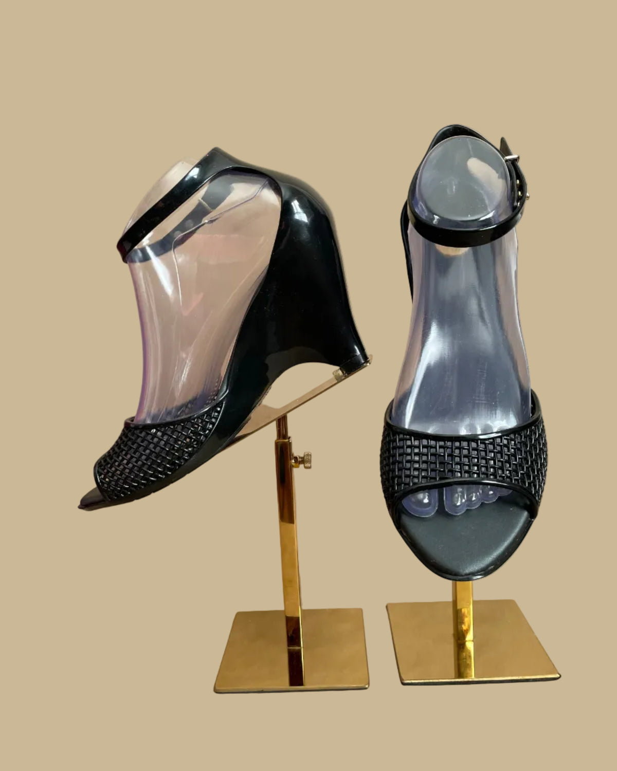A pair of black Melissa jelly wedge sandals with a woven-texture toe strap and ankle buckle, displayed on gold stands against a kraft background