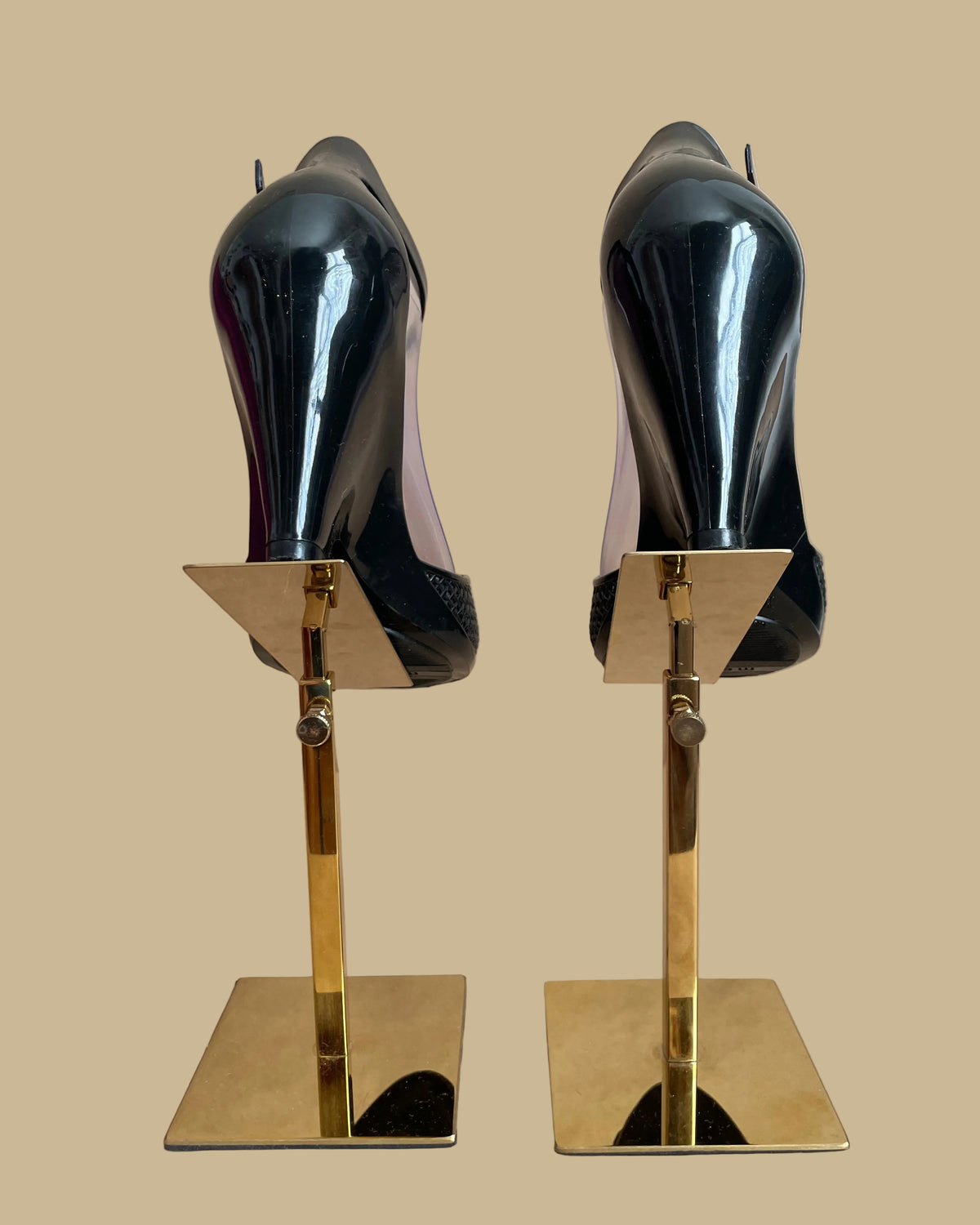 A pair of black Melissa jelly wedge sandals with a woven-texture toe strap and ankle buckle, displayed on gold stands against a kraft background