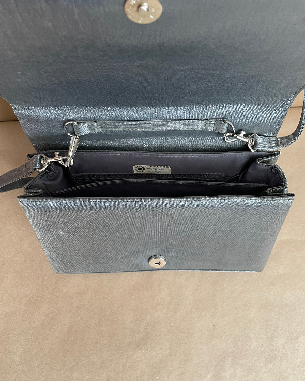 Pewter-silver metallic evening bag with a polished chrome feline handle across the flap