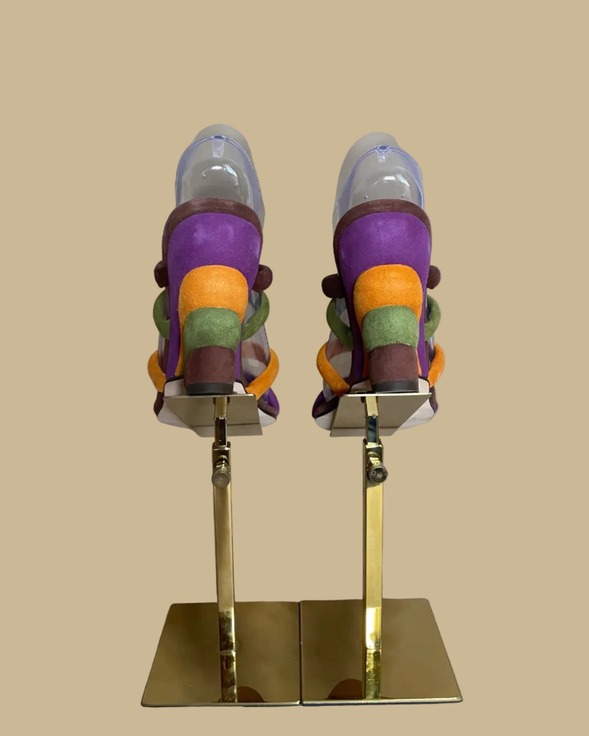 A pair of multi-strap suede wedge sandals in brown, olive, mustard, and purple, shown on clear display forms against a neutral beige background