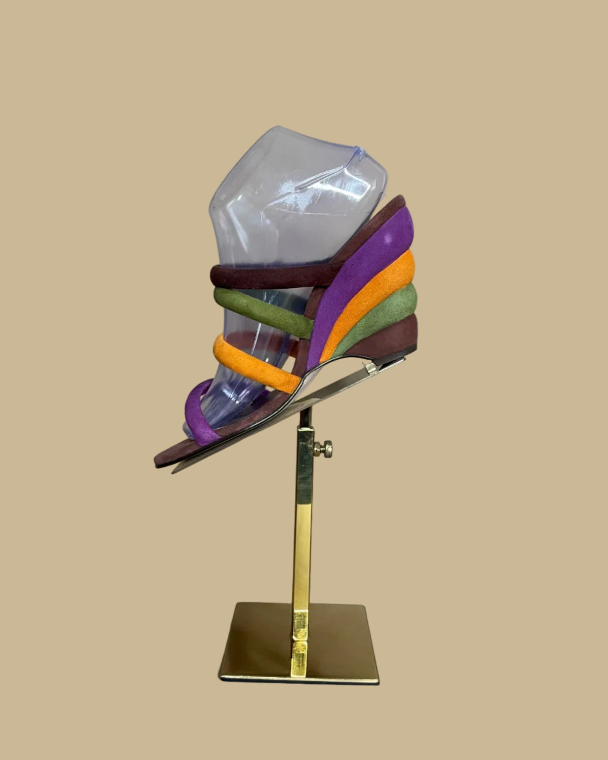A pair of multi-strap suede wedge sandals in brown, olive, mustard, and purple, shown on clear display forms against a neutral beige background