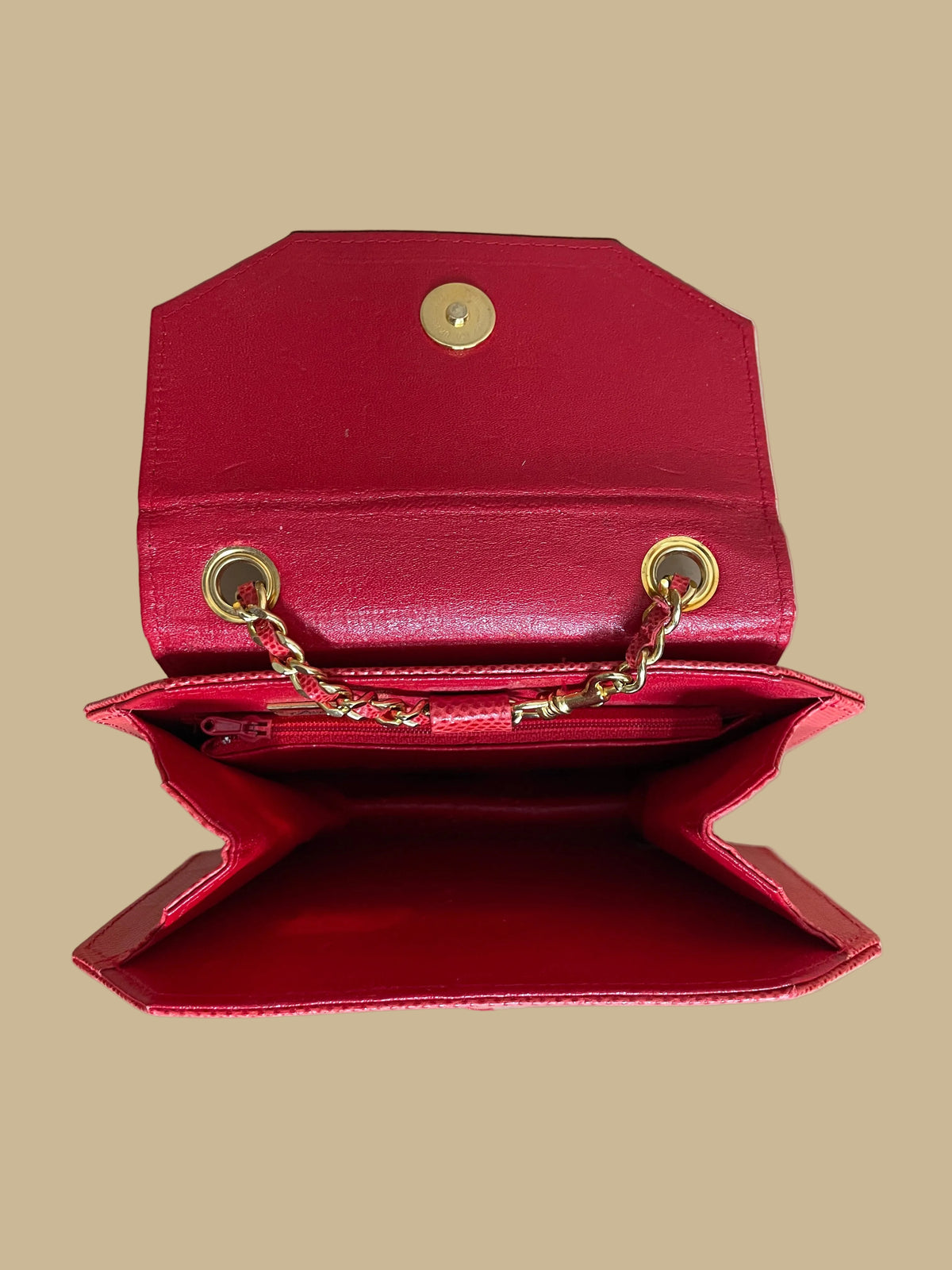 A small red textured snakeskin handbag with a gold-tone panther head clasp, shown on a neutral beige background with its matching chain strap