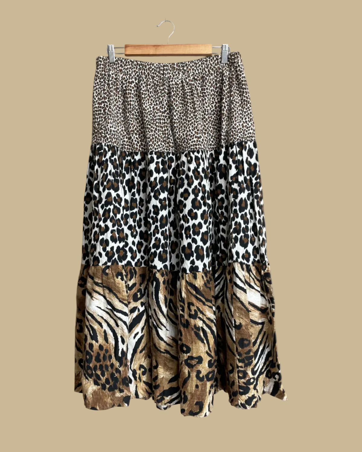 Full view of the tiered maxi skirt hanging against a neutral beige background, showing the elastic waist and flowing silhouette