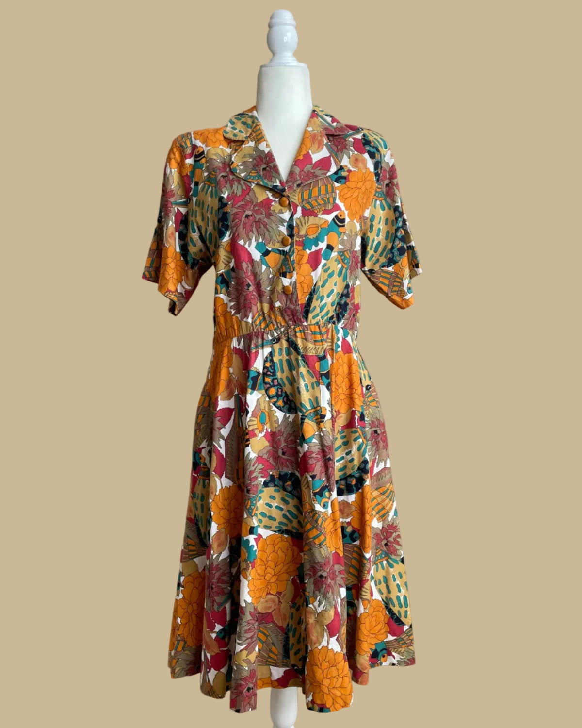 A vintage Sabino shirtdress with a bold tropical fish and floral print in mustard, teal, and coral tones, on a mannequin against a neutral beige background