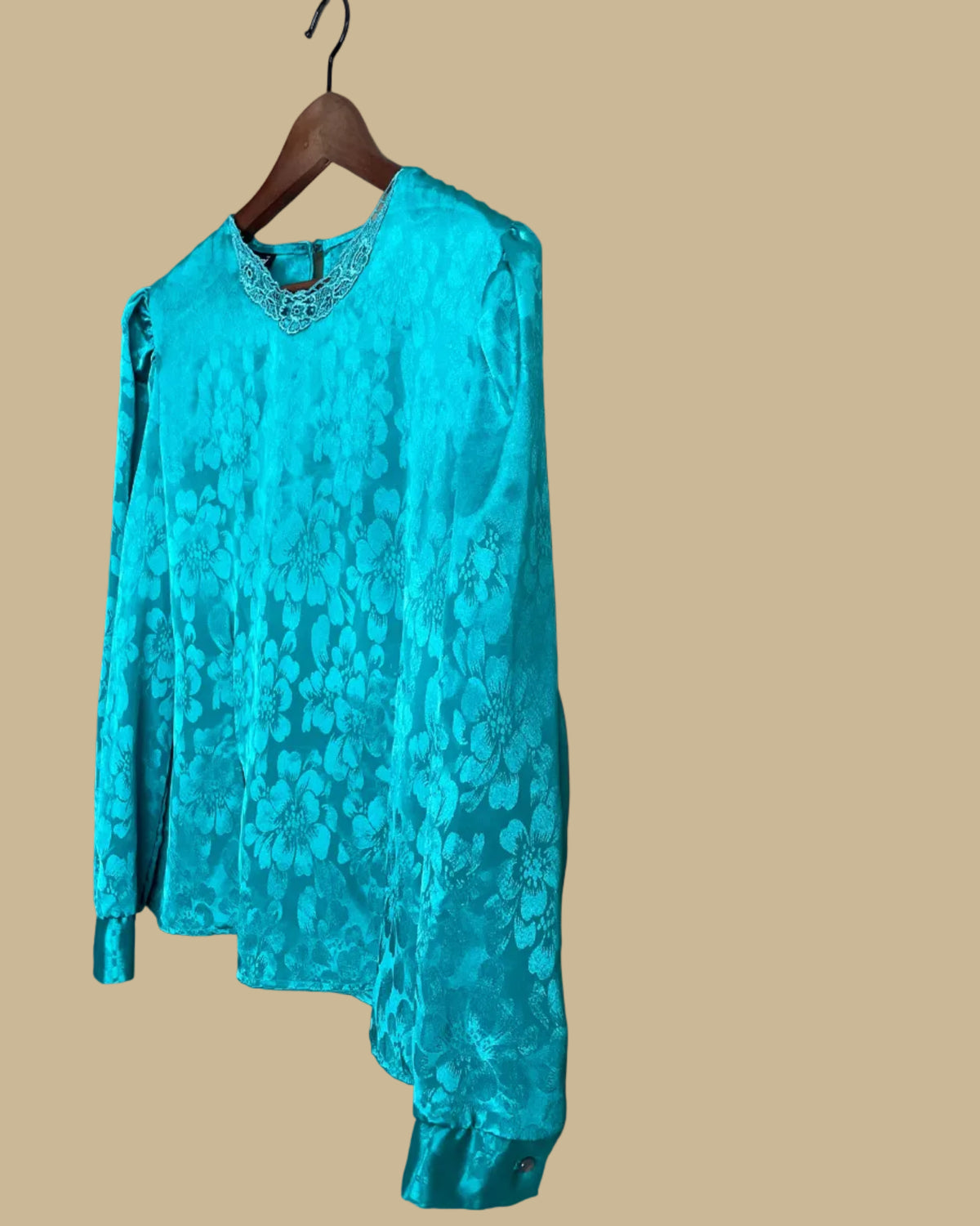 Full front view of the teal floral jacquard blouse on a hanger against a neutral beige background
