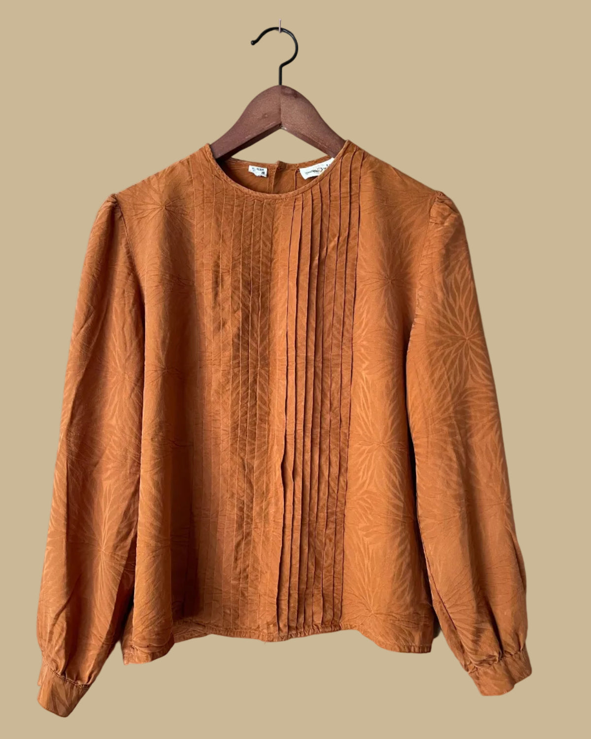Vintage Oleg Cassini rust jacquard pintuck blouse on a hanger against a beige background