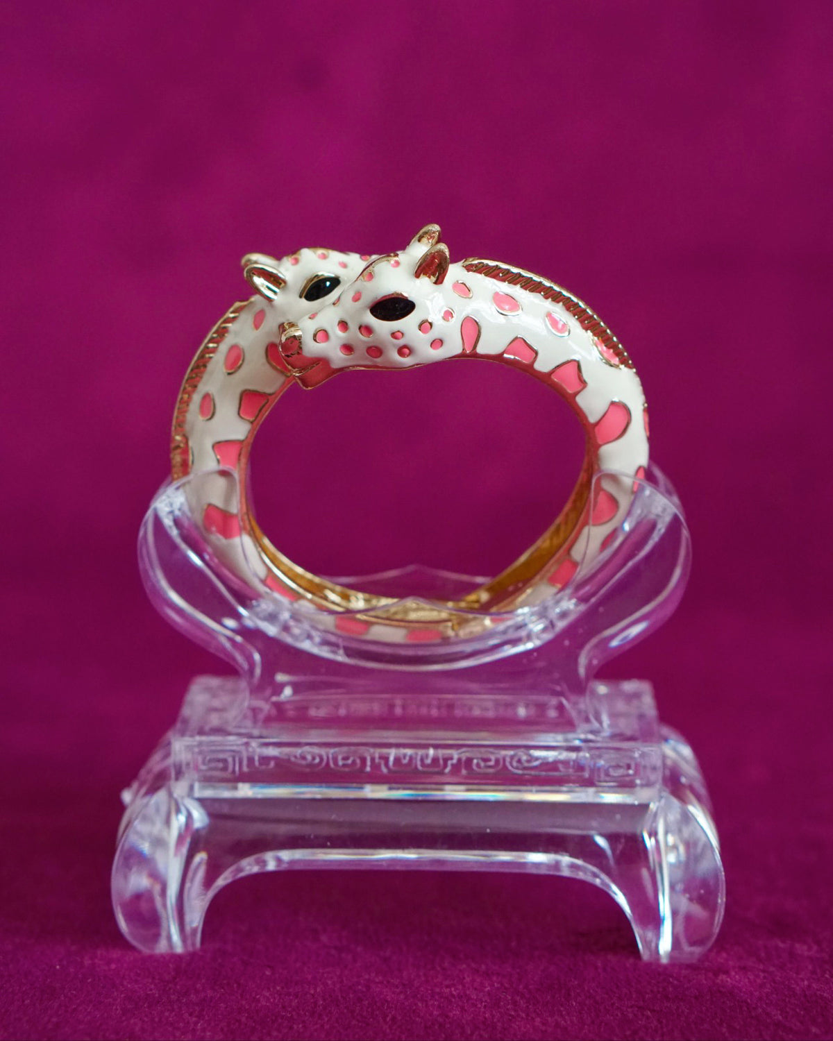 Hinged cream enamel bangle with two giraffes nuzzling at the front of the wrist, soft pink accents