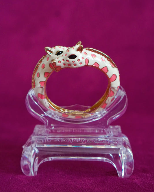 Hinged cream enamel bangle with two giraffes nuzzling at the front of the wrist, soft pink accents